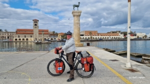 Man on a touring bicycle standing in front of a monument