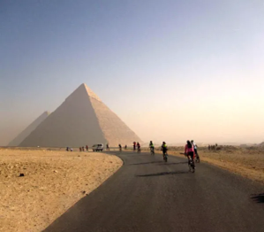 Egyptian pyramids in the background with bicyclists riding on the road