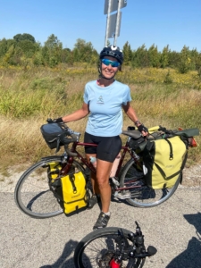 A woman in riding gear posing astride a fully packed bicycle