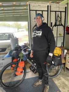 Man standing in front of a fully loaded touring bicycle