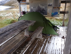 A tent pitched under a shelter in the snow next to a lake