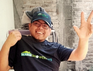 A man in a Warmshowers logo hat and t-shirt waving hello